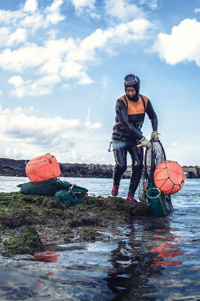 A haenyeo diver, still wearing her wetsuit, goggles, gloves and vest,  pulls up her net and flotation device after a dive off the coast of Jeju Island in Korea. 