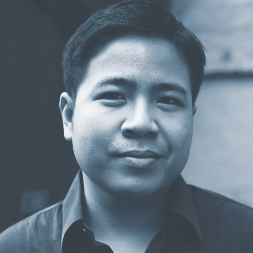 A greyscale photo of author Pitchaya Sudbanthad shows a close-up of his face, looking directly at the camera. 
