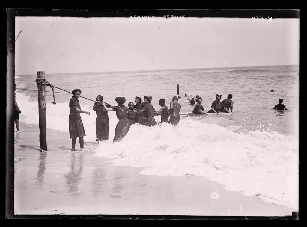 This 1908 photograph, titled “Negroes, Asbury,” depicts a group of African Americans playing in the waves at the beach in Asbury Park, New Jersey.