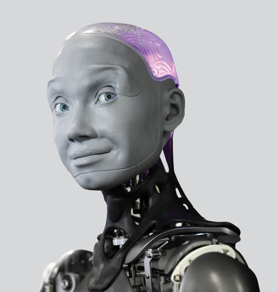 The Engineered Arts Ameca humanoid robot stares at the camera, with a slate-grey humanoid face, blue eyes, and mechanical neck and shoulders. 