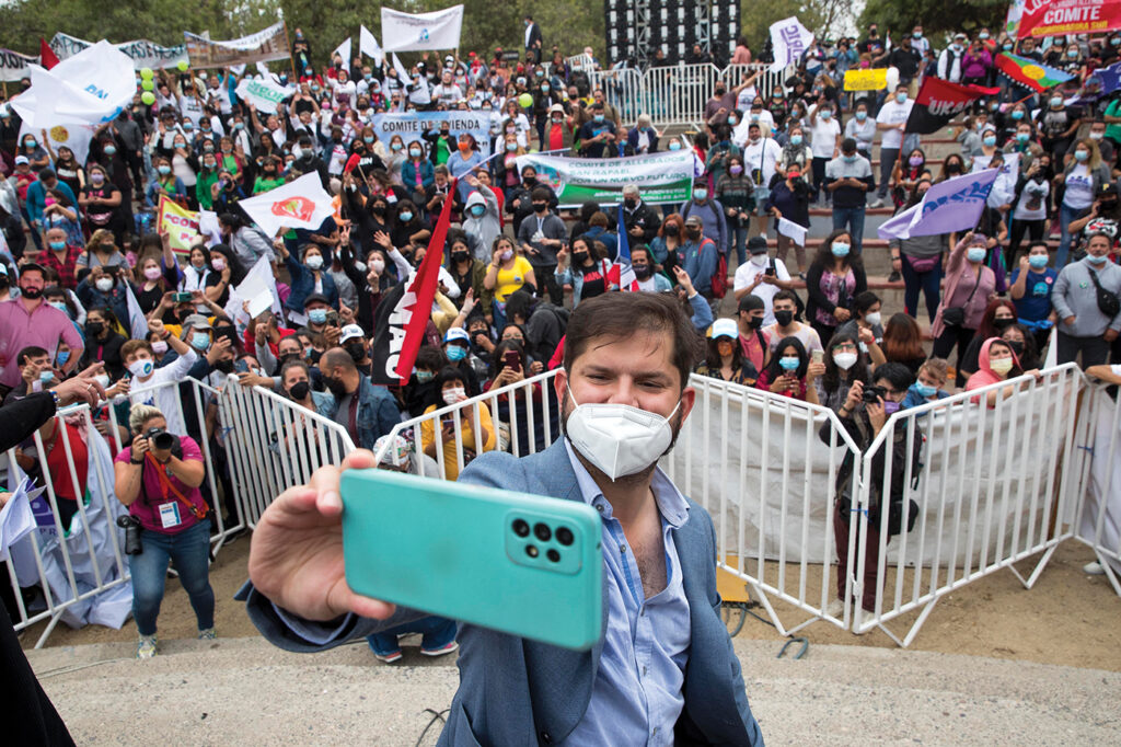 Gabriel Boric, wearing a mask, takes a selfie in front of a group of supporters. 