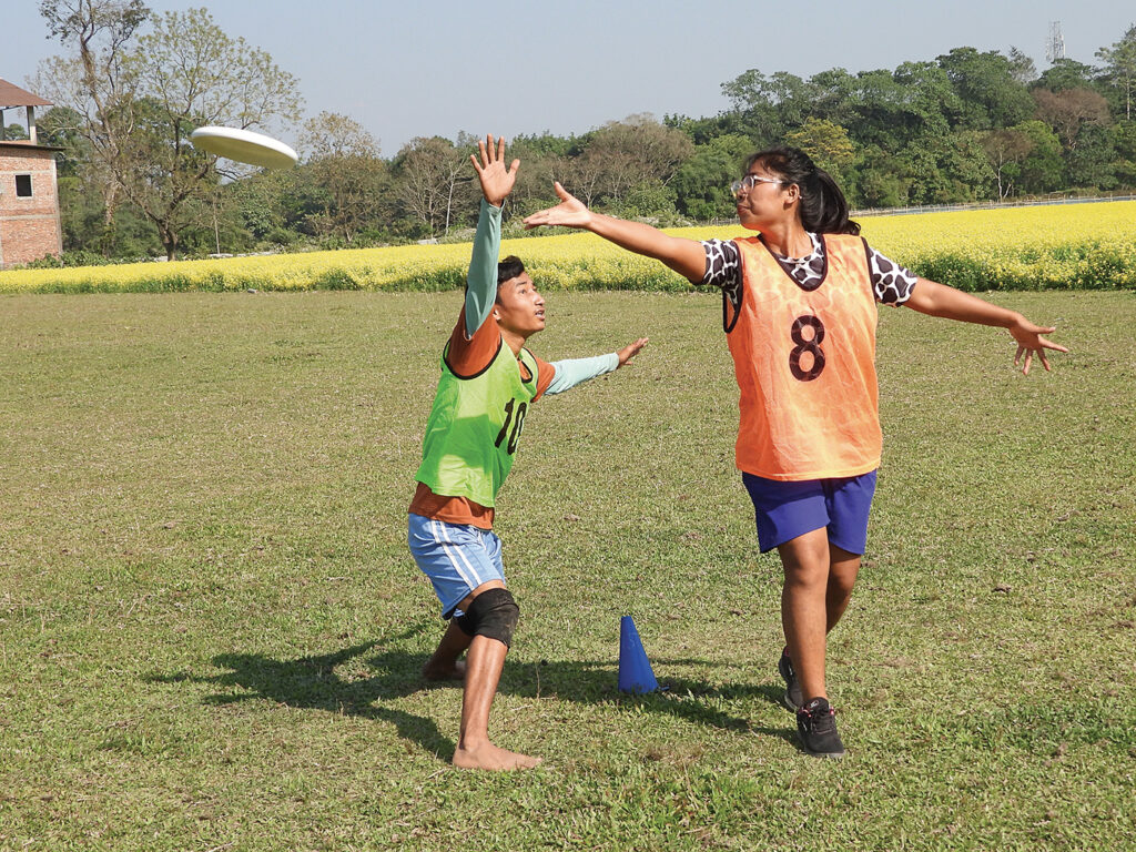 Two young people, a boy and a girl, wearing practice jerseys practice Ultimate moves in a field