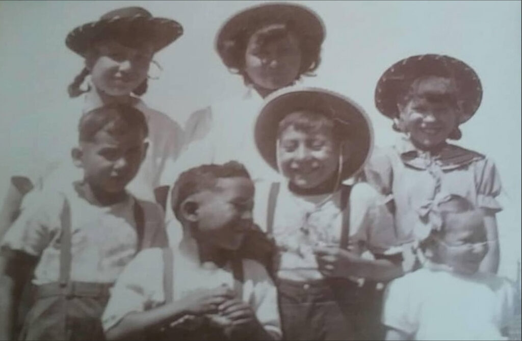 An old, black and white photograph from 1950 depicting six siblings, all smiling. There are three older girls, three boys, and one young sister. 