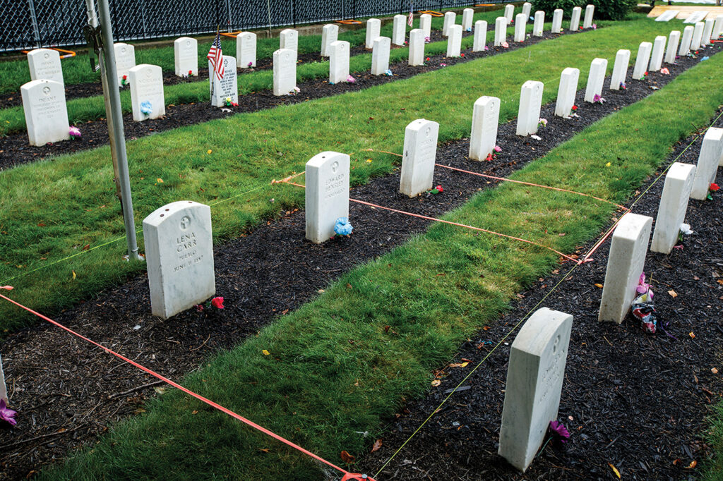 A photograph in a graveyard with identical white stones. Some of the graves have been marked off with string. 