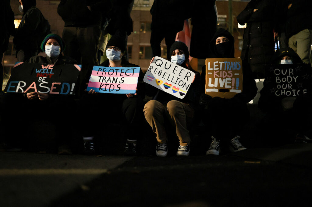 After Trump’s executive order on Jan. 28, 2025, that restricted gender transition procedures for people under the age of 19 and a local hospital cancelled scheduled appointments, hundreds demonstrated in protest in New York City on Feb. 3, 2025. Here, five protesters seated next to one another hold signs like "We will not be erased" and "protect trans kids." 