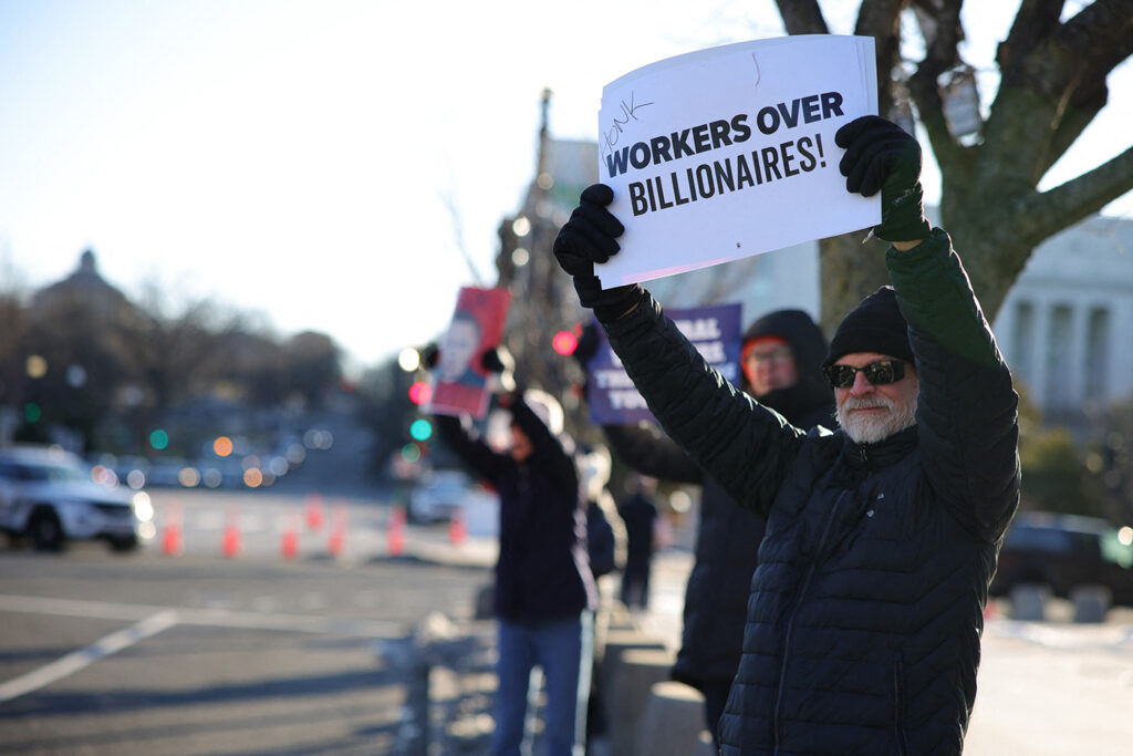 On Feb. 14, 2025, demonstrators gathered outside of the offices of the Department of Health and Human Services in Washington, D.C., to protest against Elon Musk’s Department of Government Efficiency budget cuts and employee terminations. One man holds a sign that reads "Workers over billionaires!" 