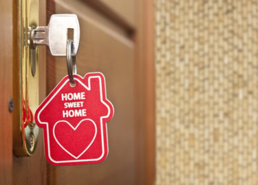 Key in lock with "Home Sweet Home" keychain. Photo by Shutterstock.